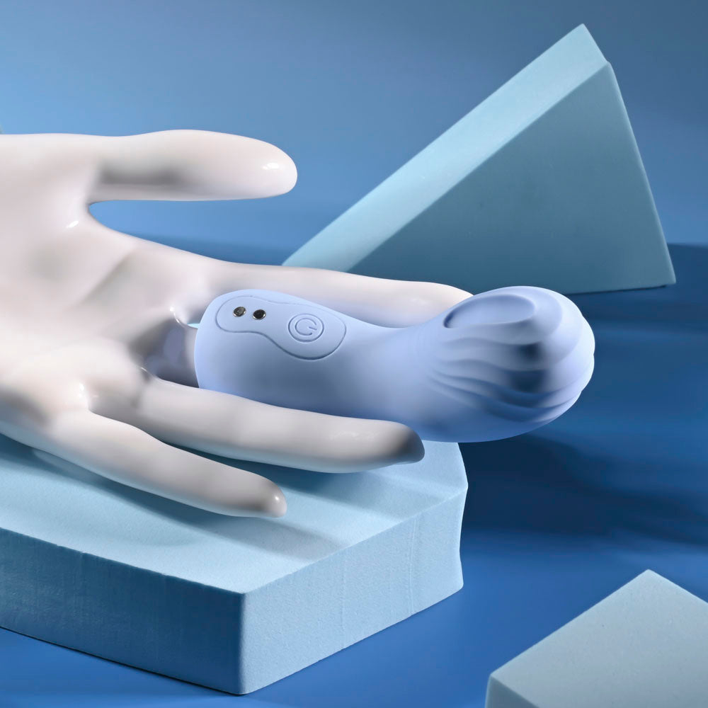 A light blue silicone finger vibrator with a textured tip rests on a white hand-shaped object.