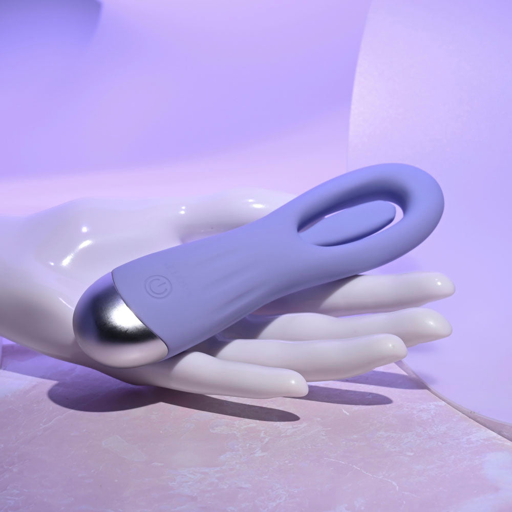 A purple silicone G-spot vibrator with a silver tip rests on a white mannequin hand.