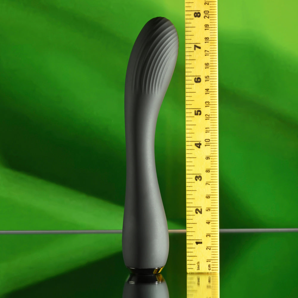A gray, curved silicone vibrator with ridges on top, measured against a ruler.