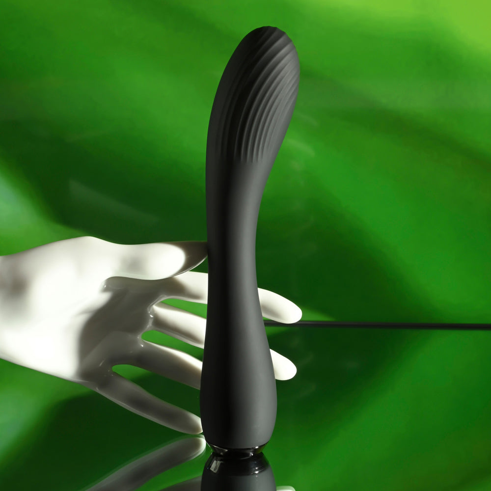 Black curved silicone vibrator with textured head held by a white mannequin hand.