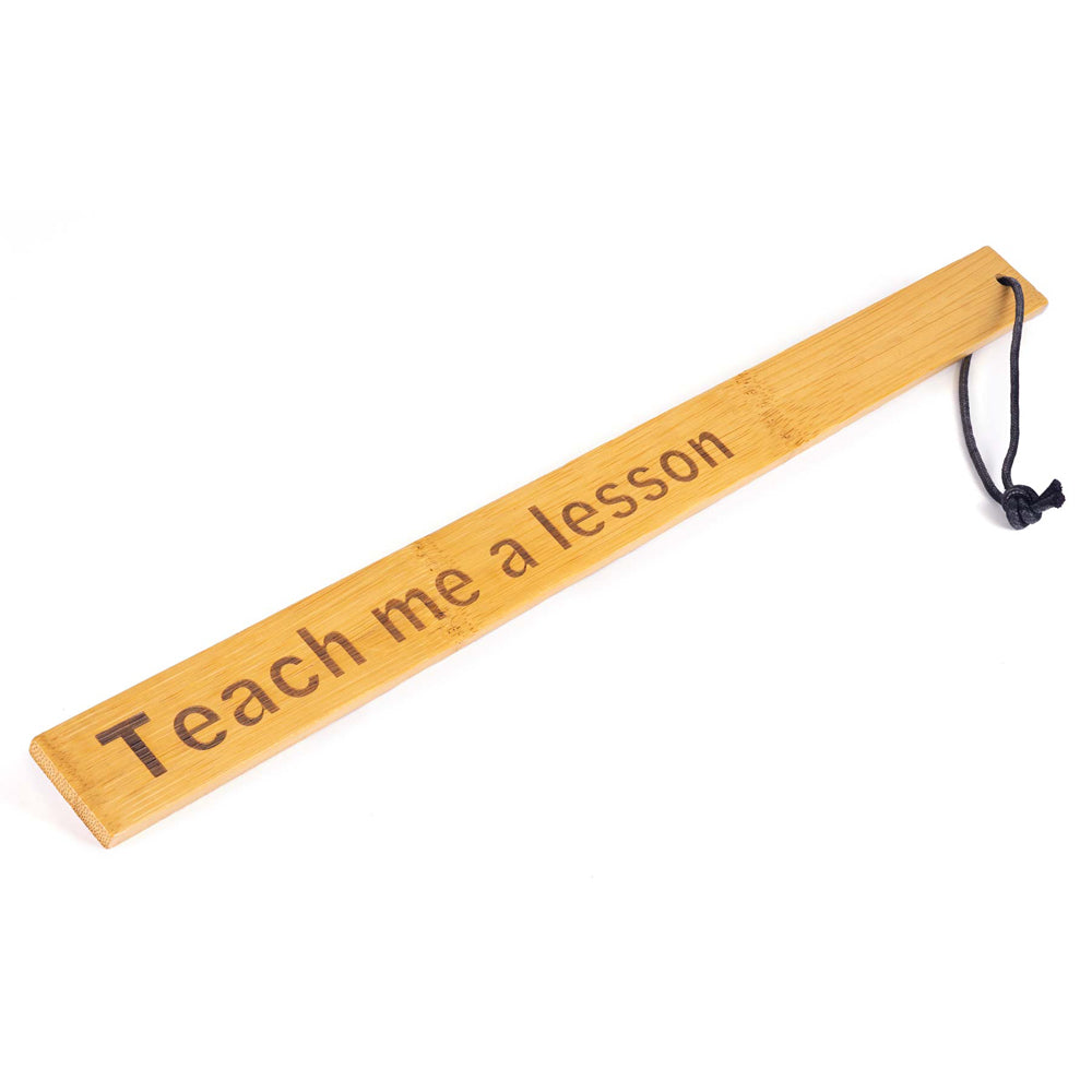 Bamboo paddle ruler with "Teach me a lesson" engraved and a black string.