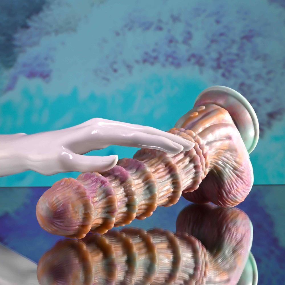 A white hand touches a ribbed, pink and orange dildo with a flared base.