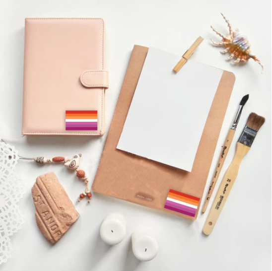 Lesbian sunset flag stickers on a pink planner and brown notebook.