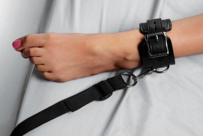 Black padded PU leather ankle cuff with strap attached to a metal ring.