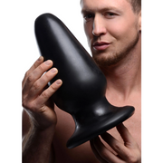 Black PVC Gigantor XXXL tapered anal plug held by a man.