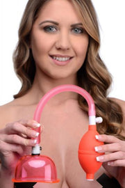 A woman holds a vaginal suction pump with a pink hose and orange bulb.