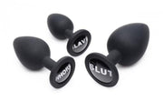 Three black silicone anal plugs with "Slave", "Whore", and "Slut" inscribed on them.