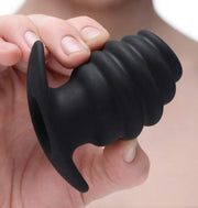 Black ribbed hollow silicone anal tunnel plug held by fingers.