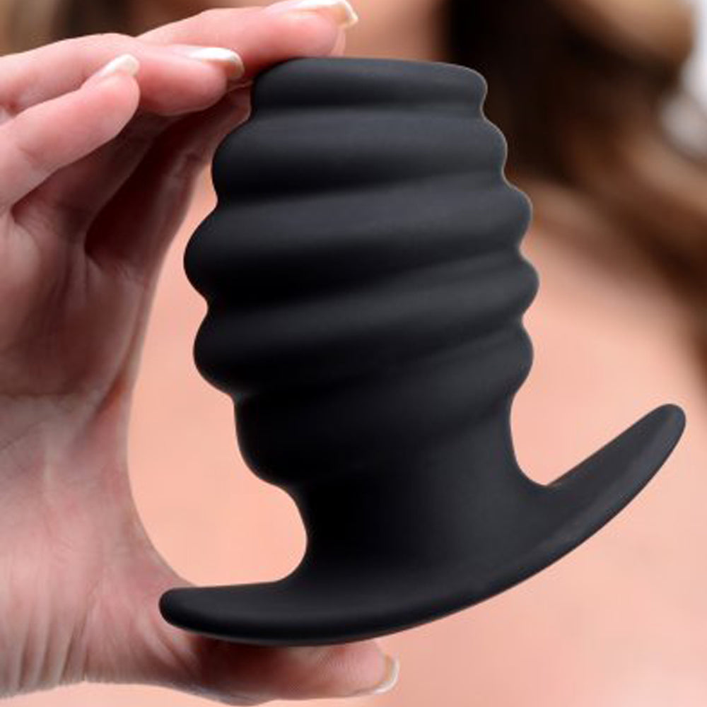 Black ribbed hollow silicone anal tunnel plug held by a hand.