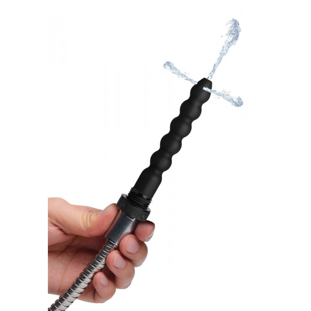 A hand holds a black silicone enema nozzle attached to a shower head, with water spraying from the nozzle.