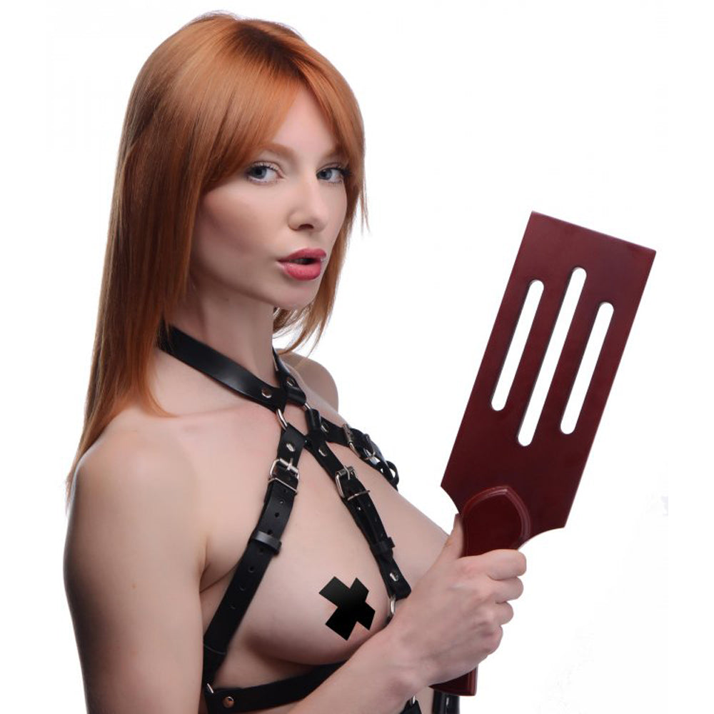 Woman in black harness holding a wooden paddle with slots.