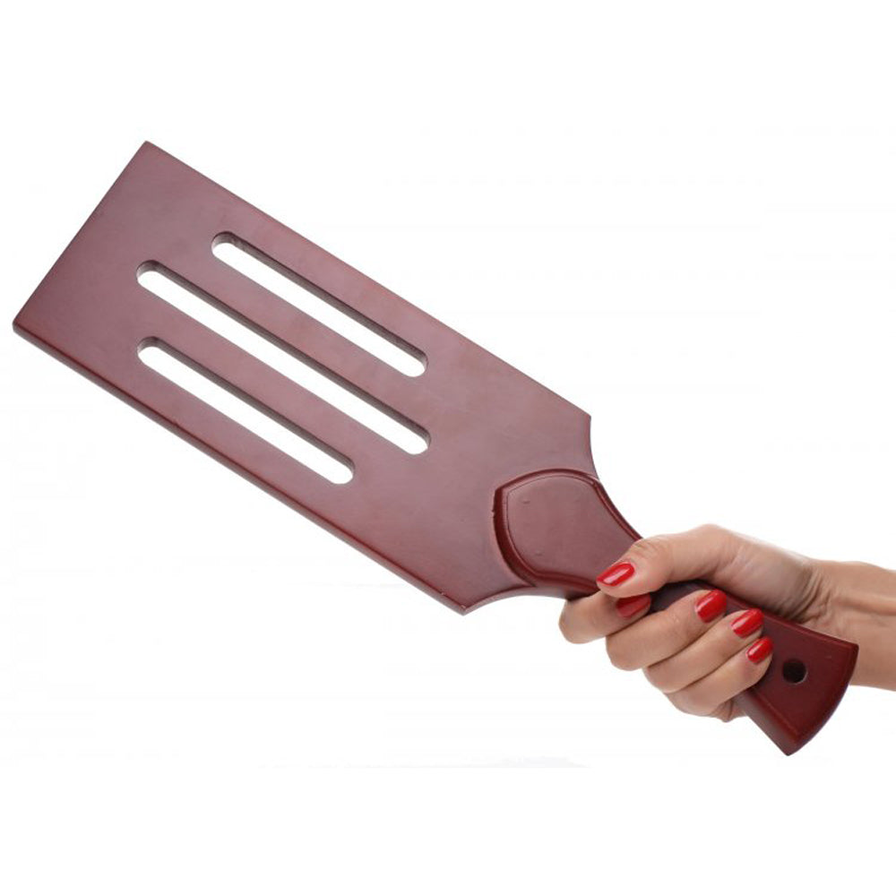 A hand holds a wooden paddle with three slots and a curved handle.