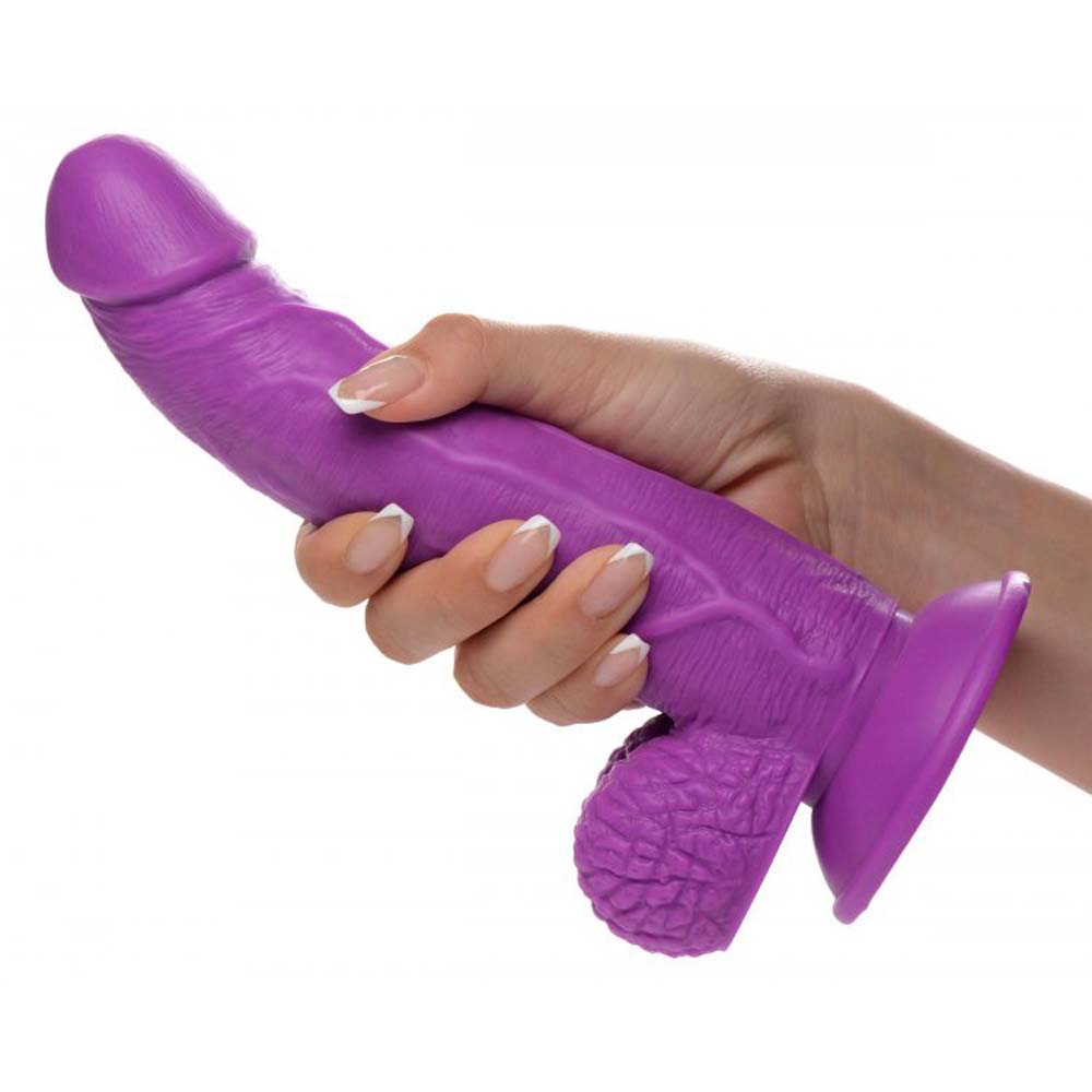 Purple realistic PVC dildo with veiny shaft, balls, and suction cup base, held in hand.