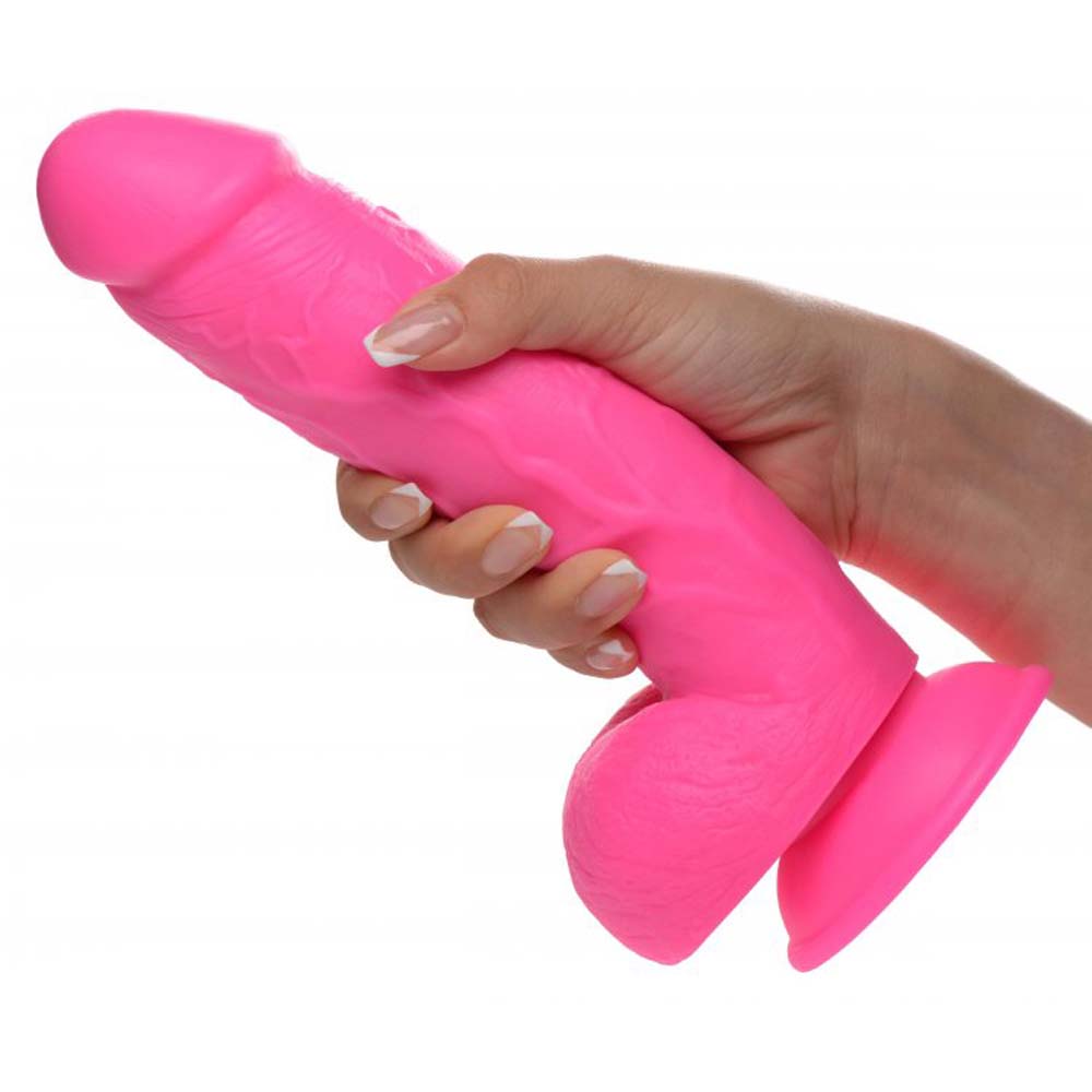 A pink realistic suction cup dildo with balls, held in a hand.