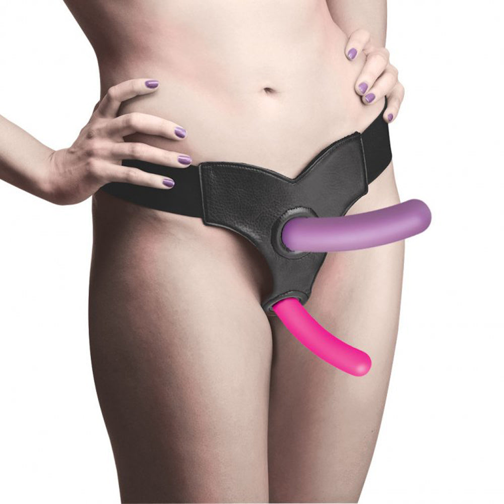 Black leather harness with purple and pink silicone dildos attached, modeled on a nude woman.