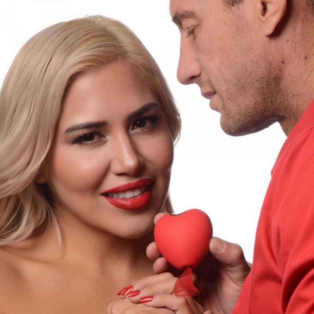 A red heart-shaped clitoral suction toy held by a couple.