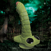 A green, scaly dildo with a pink tip and black eyes on a suction cup base.
