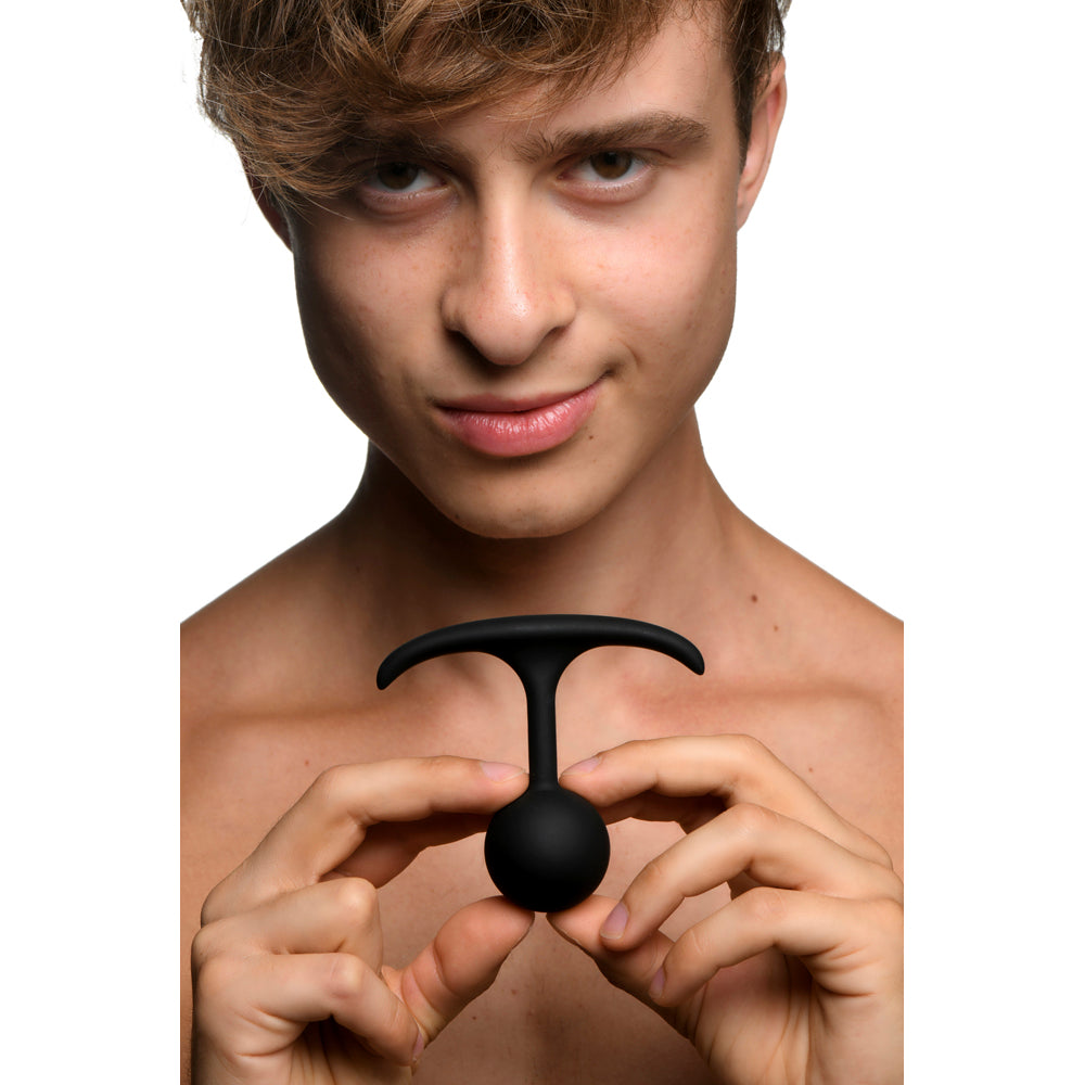 A young man holds a black, T-shaped weighted silicone anal plug.