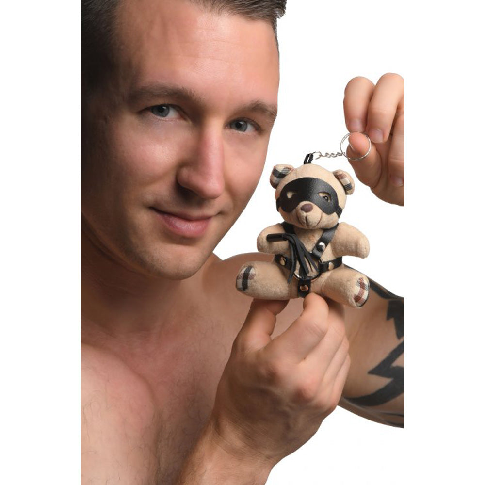 A teddy bear keychain with a faux leather harness and mask.