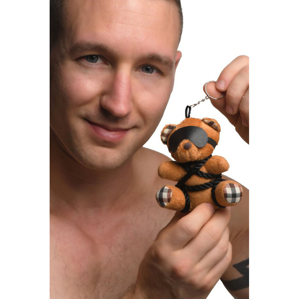 Burnt orange teddy bear keychain with black blindfold and rope details.