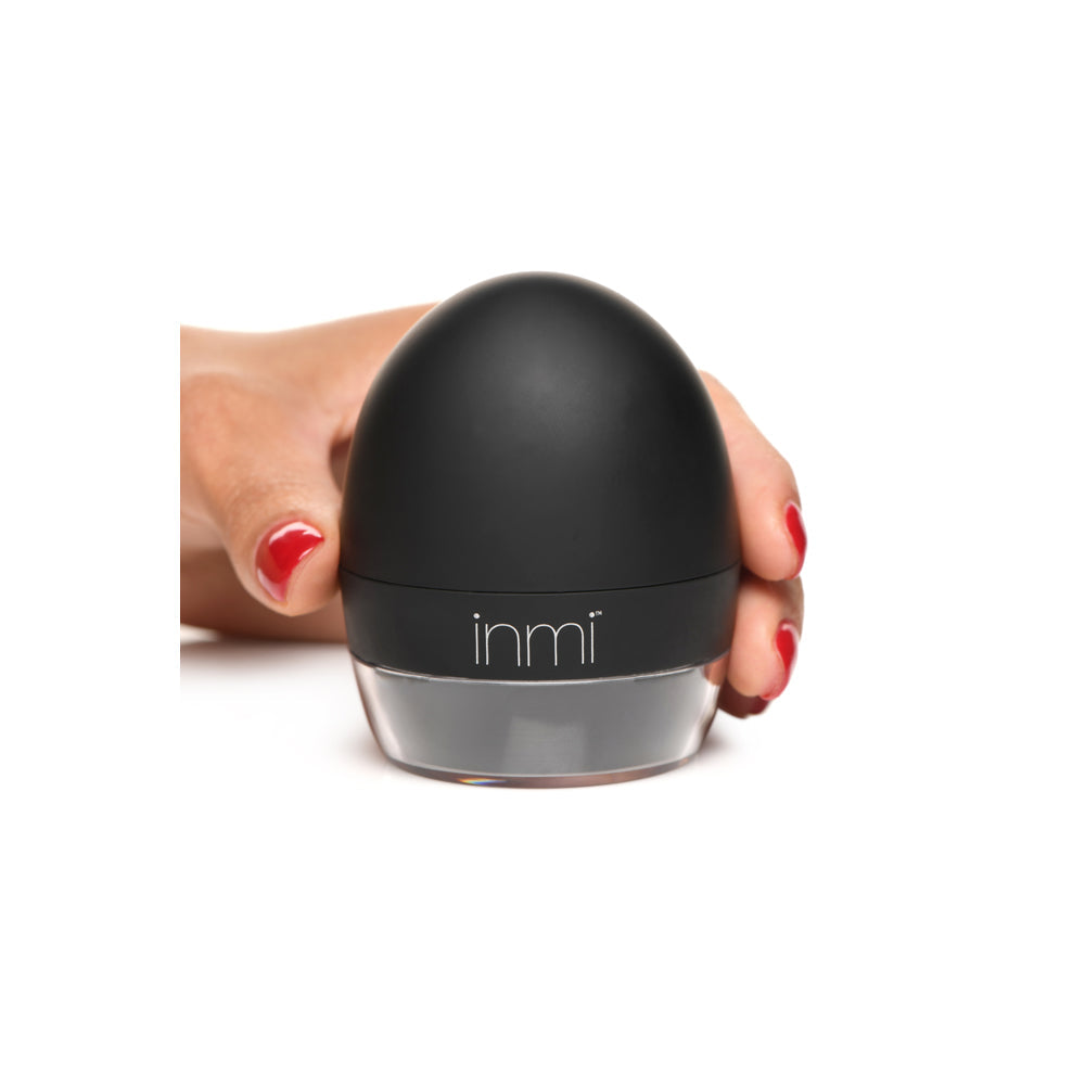 A hand holds a black, egg-shaped oral stimulator with a clear base.