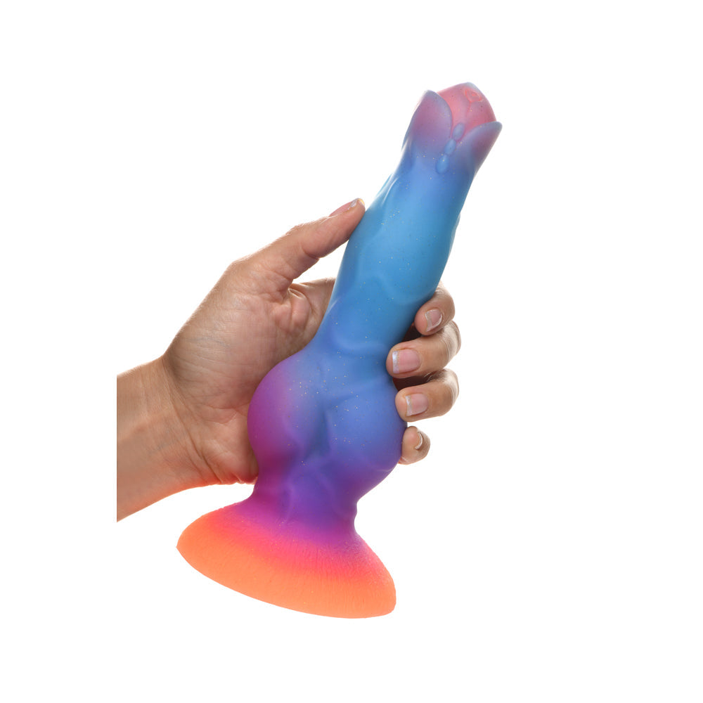 A hand holds a colorful, glow-in-the-dark dildo with a suction cup base.