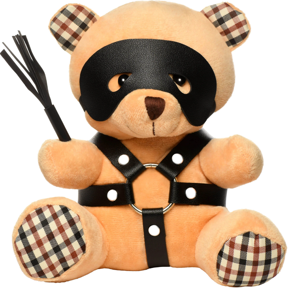 A plush teddy bear wearing a black eye mask and faux leather harness, holding a mini flogger.