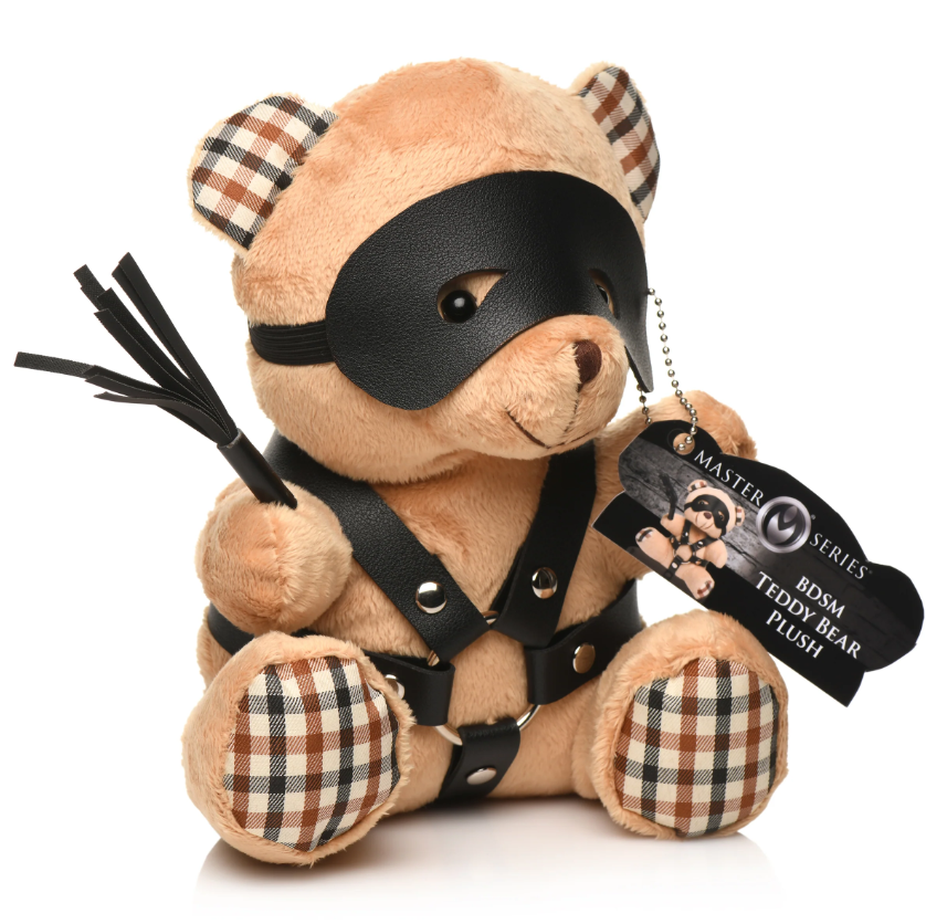 A teddy bear wearing a black faux leather harness, eye mask, and holding a small flogger.