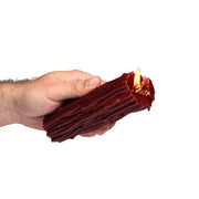 A hand holds a red, thorn-shaped candle with a lit wick.