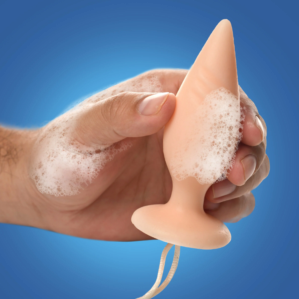 A peach-colored butt plug shaped soap on a rope with foam.