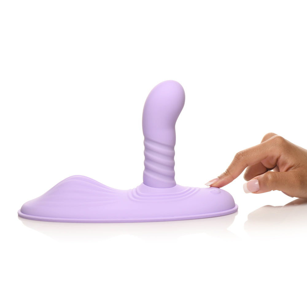 A purple silicone grinding pad with a ribbed stimulator and a hand pressing a button.