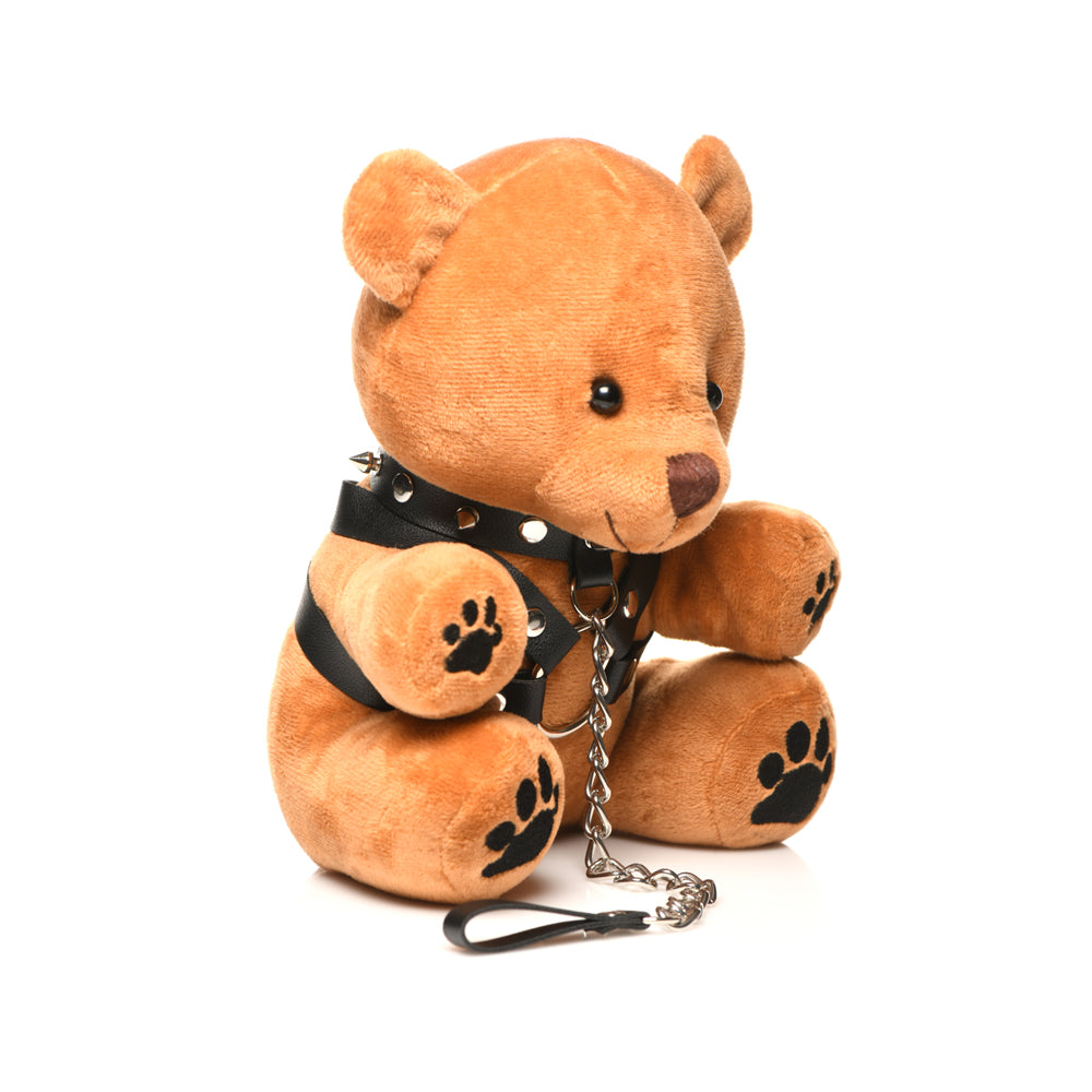 A brown teddy bear wearing a black spiked collar, harness, and leash.