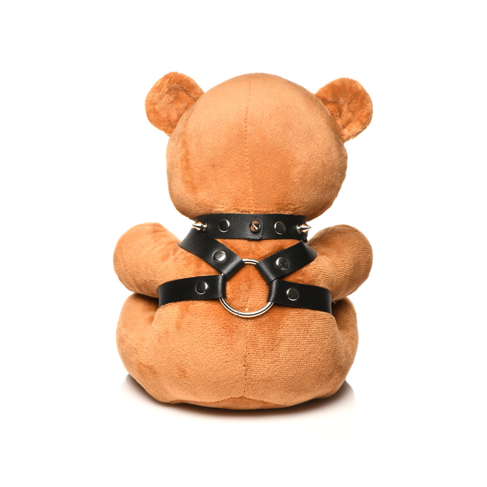 A plush teddy bear wearing a black spiked collar and harness with a metal ring.