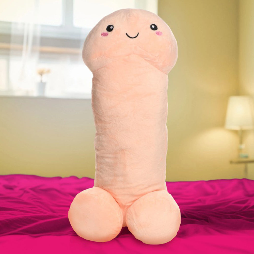Large plush penis-shaped pillow with a smiling face on a pink bed.