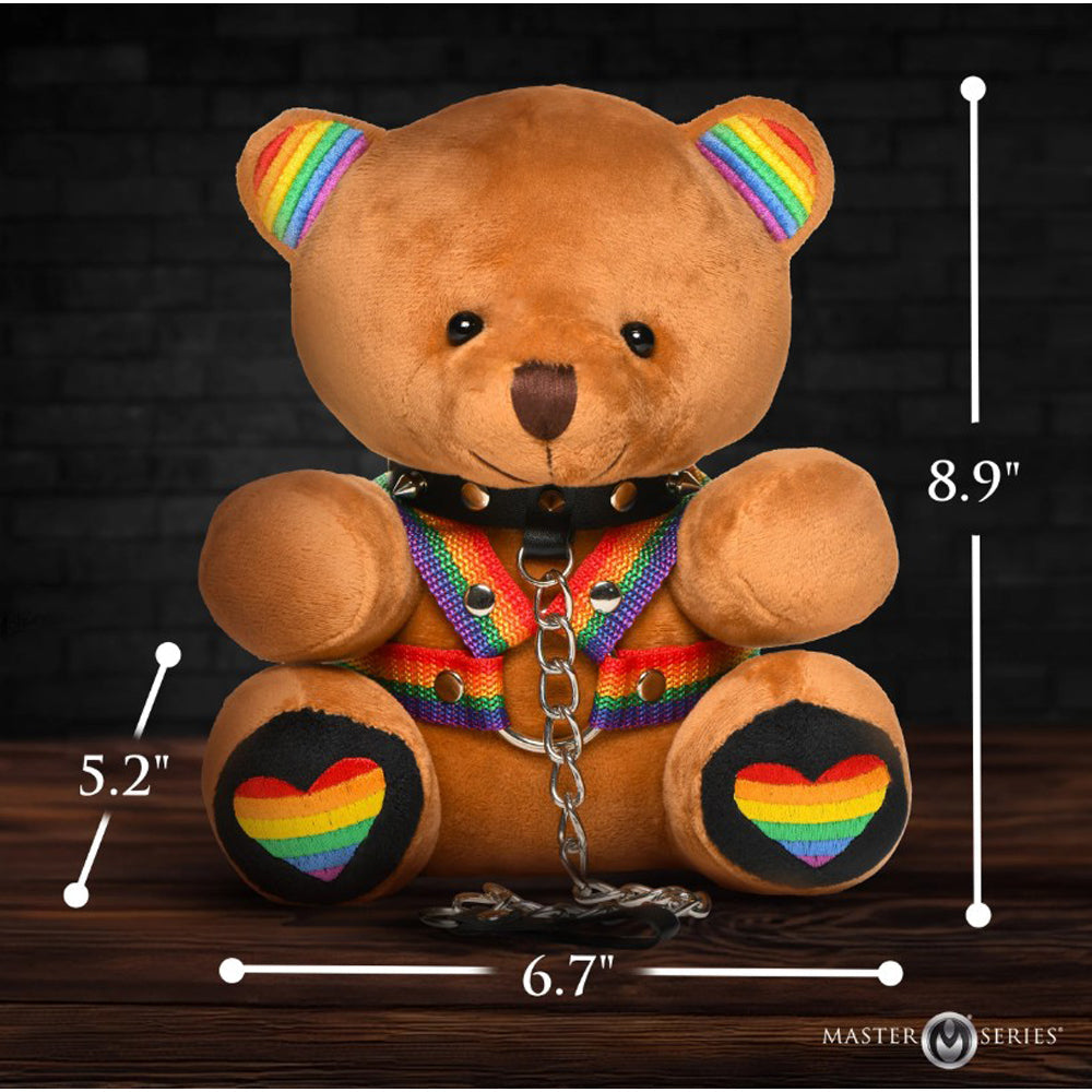 A brown teddy bear with rainbow accents on its ears, harness, and feet, wearing a spiked collar and leash.