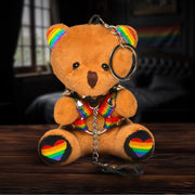 A plush teddy bear keychain with rainbow accents, a spiked collar, and a harness.