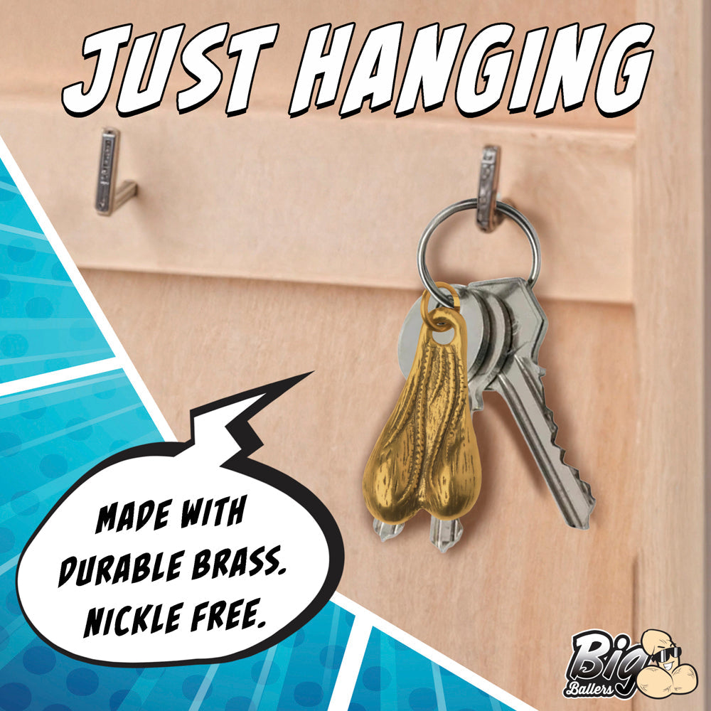 A brass novelty keychain shaped like testicles hangs from a hook with keys.