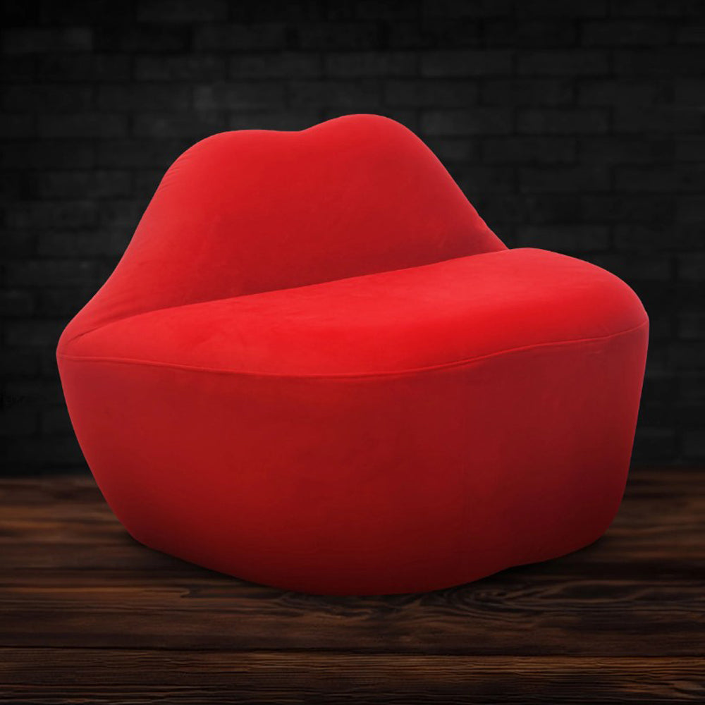 Red velvet loveseat shaped like lips on a wooden floor.