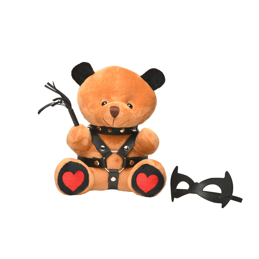 A teddy bear wearing a studded harness and holding a whip, with a mask nearby.