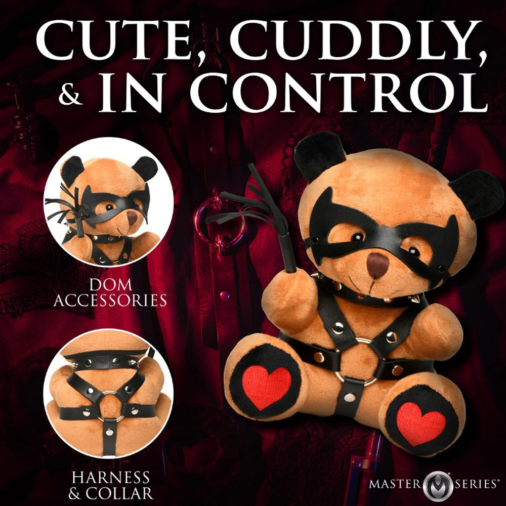 A teddy bear with a black mask, studded collar, and harness, holding a whip.