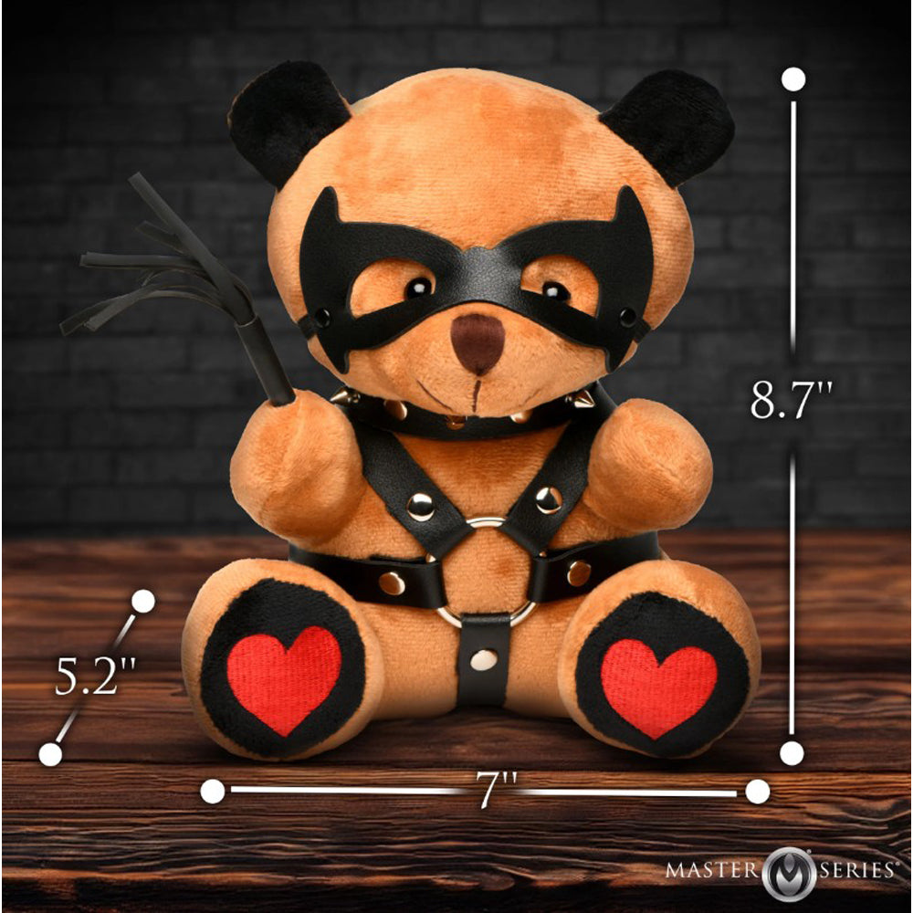 A brown teddy bear wearing a black mask and harness, holding a whip.