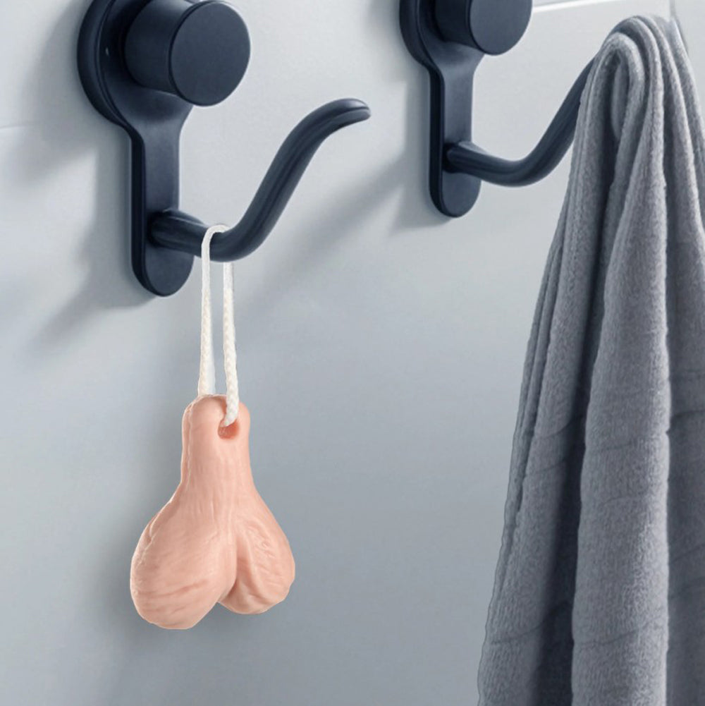 A pink, ball-shaped soap on a rope hangs from a black hook next to a gray towel.