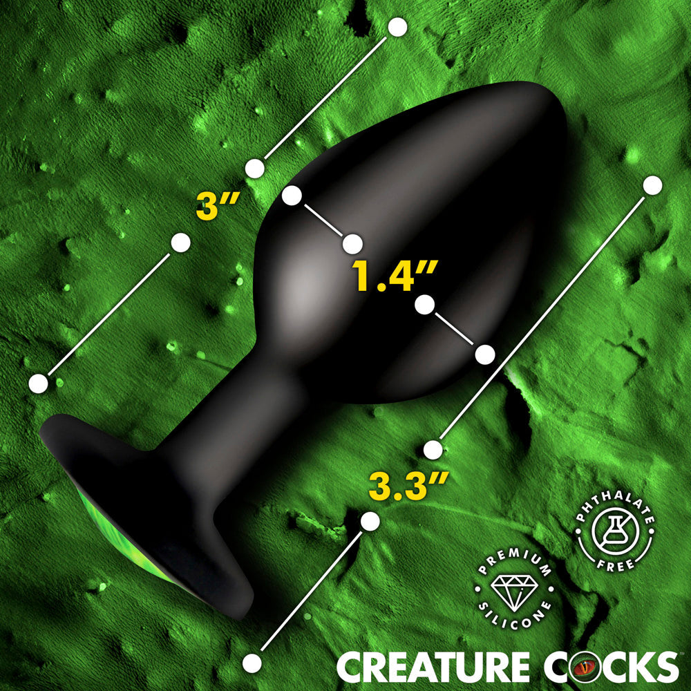 Black silicone anal plug with green creature eye detail, 3.3 inches long.