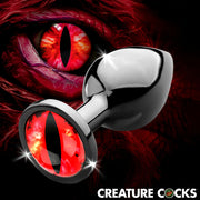 A metal anal plug with a red sinister eye design and a matching eye in the background.