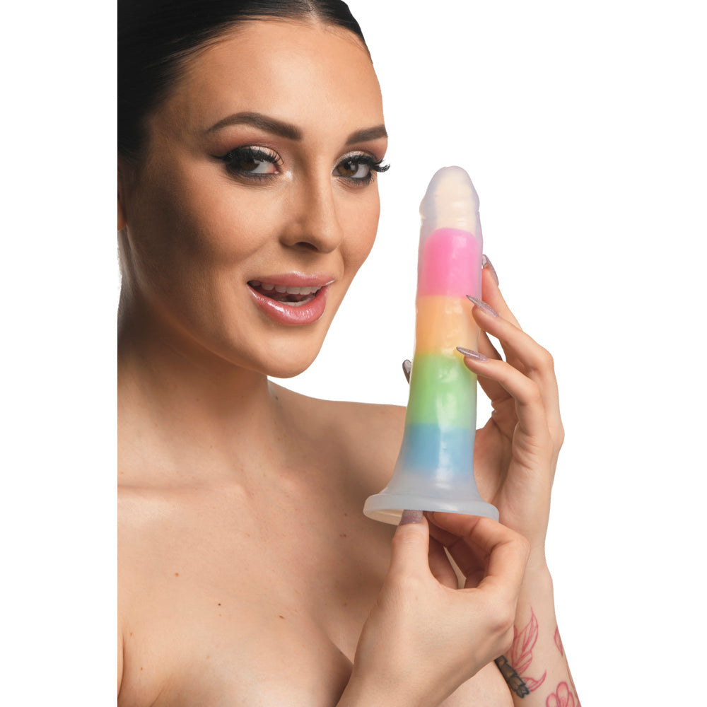 A woman holds a 7-inch glow-in-the-dark rainbow silicone dildo with a curved shape and suction base.