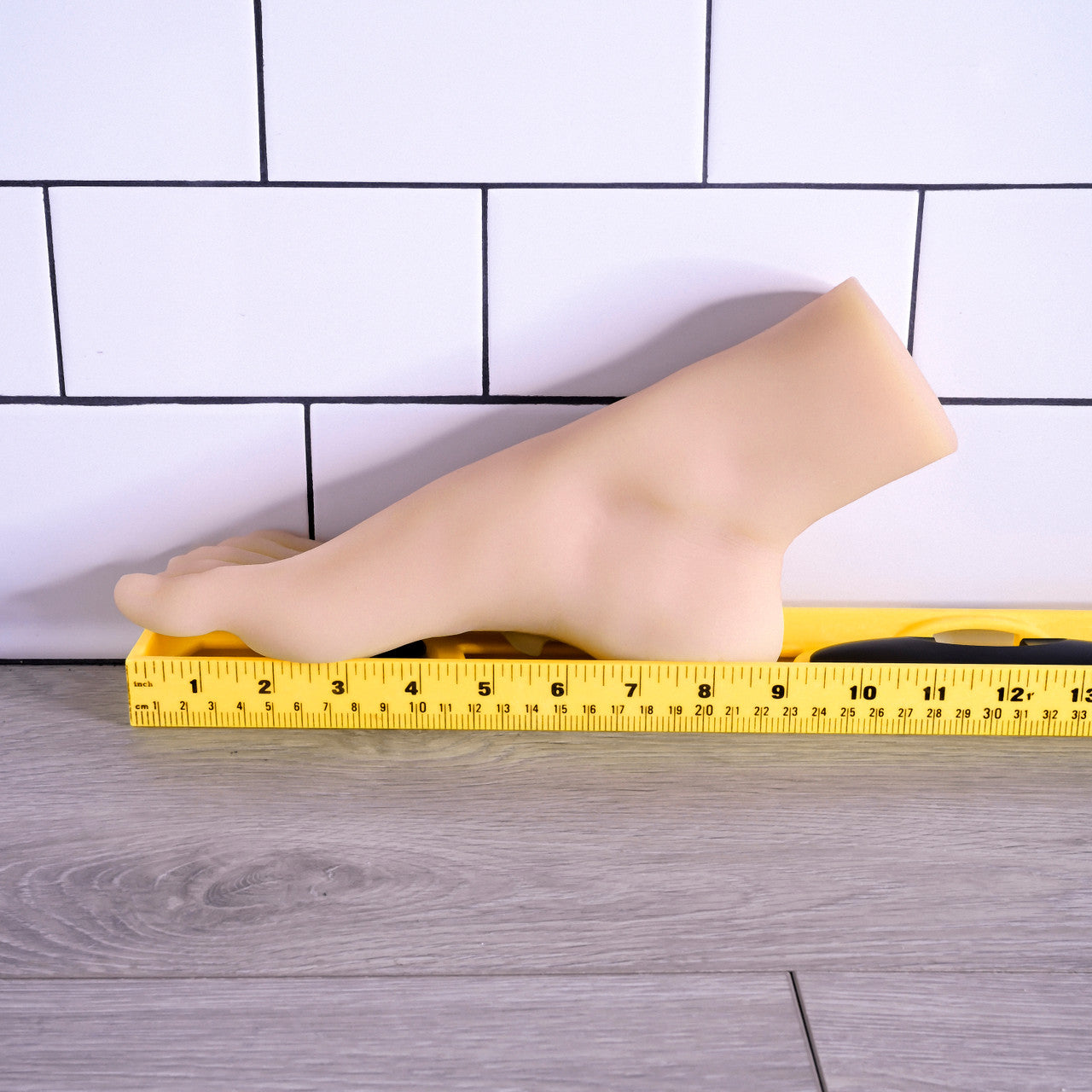 Realistic TPE foot fetish toy with lifelike toes and arch on a ruler.