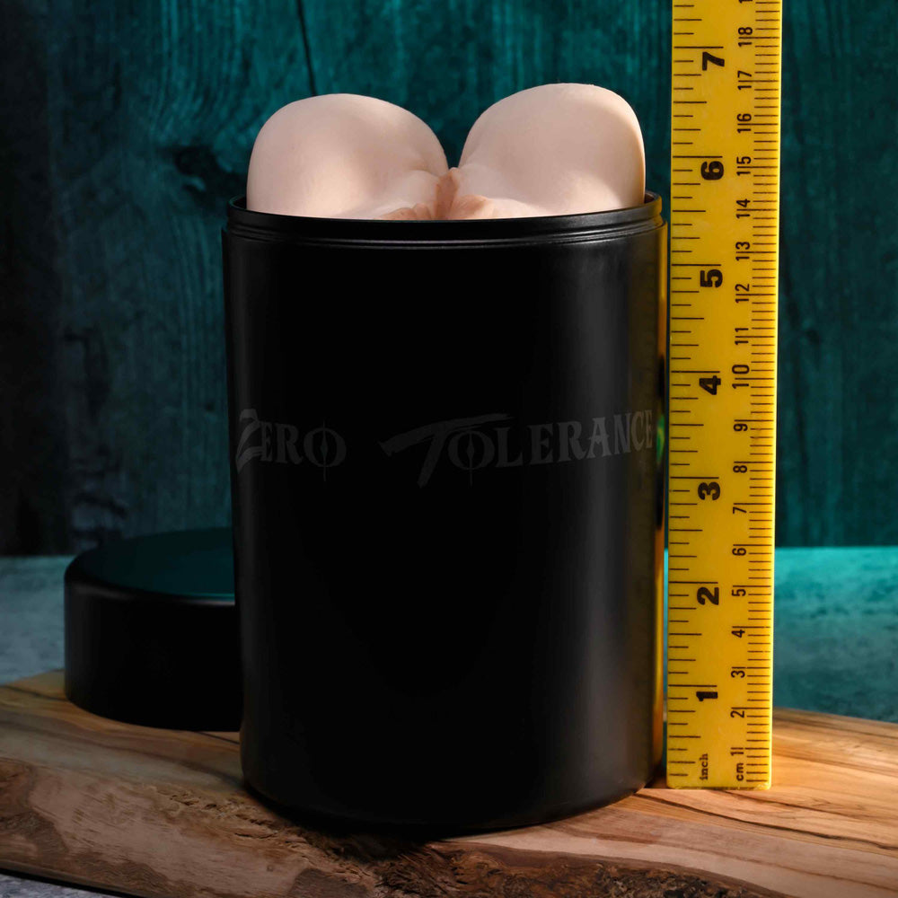 A black stroker with "Zero Tolerance" branding sits in a waterproof canister next to a ruler.