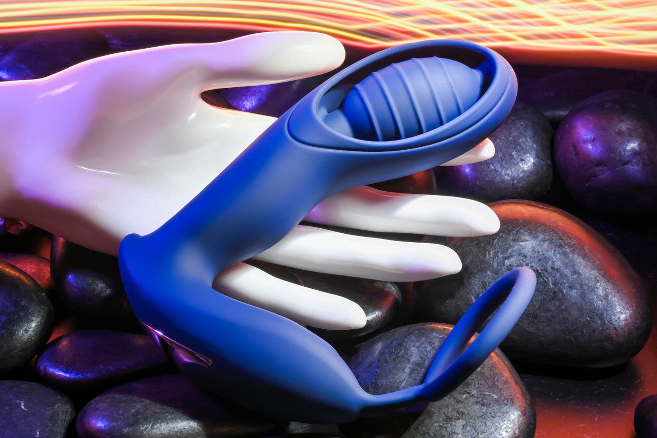 Blue C-ring vibrator with ribbed tip resting on a white hand and dark stones.