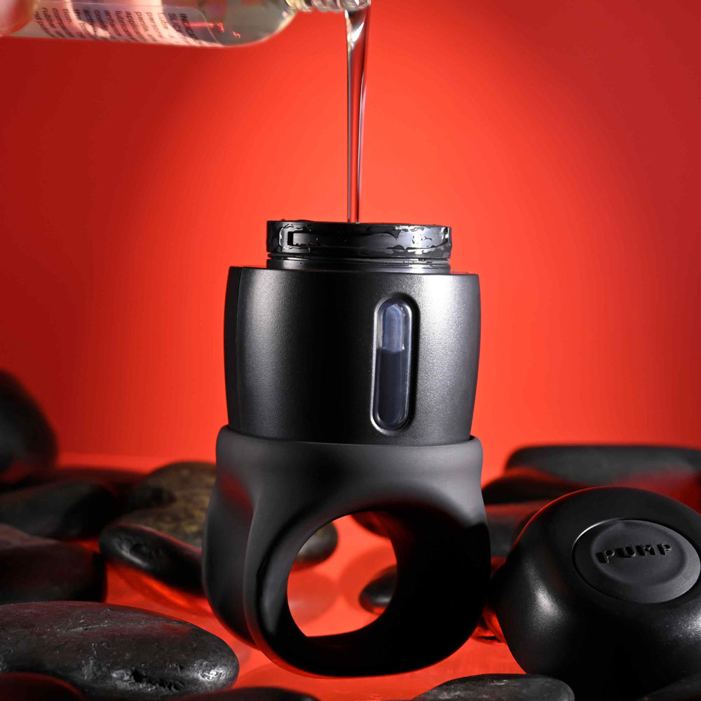 Black vibrating stroker with lube dispenser and ring, surrounded by stones.