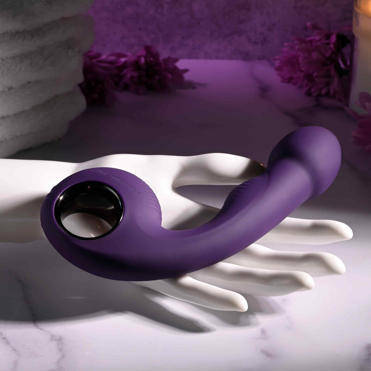 A purple silicone vibrator with a ringed handle rests on a white hand-shaped stand.